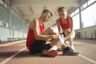 Coureur assis sur un banc, main posée sur son tibia douloureux, illustration médicale du sport